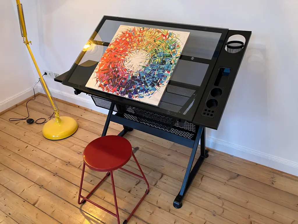 Schwarzer Zeichentisch mit buntem Kunstdruck und rotem Hocker