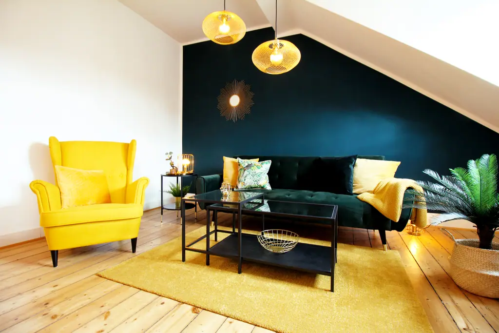 Wohnzimmer des Boho ARTstudio unter dem Dach: gelber Ohrensessel, dunkelgrünes Sofa, Holzbalken