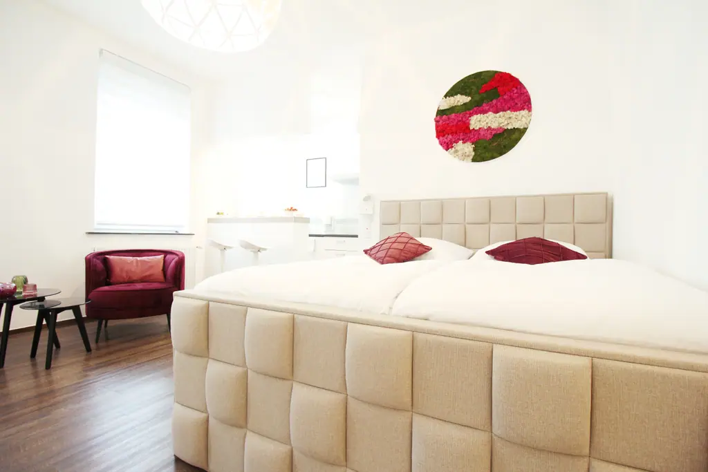 cozy 2.0: beiges Polsterbett mit roten Kissen und rundem Wandbild