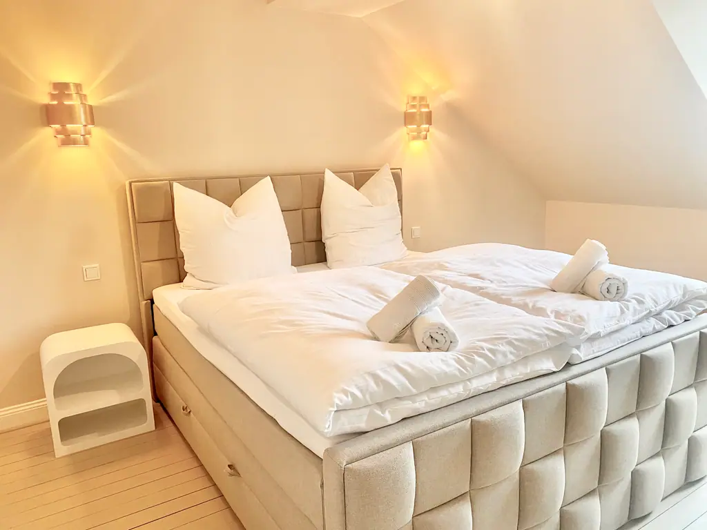 Schlafzimmer mit gepolstertem Bett und weißer Bettwäsche
