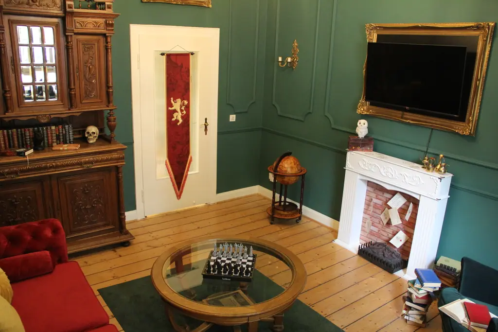 Wohnzimmer des Magic Hideaway in dunklem Grün mit Bücherschrank, Kamin, Globus und Schachtisch