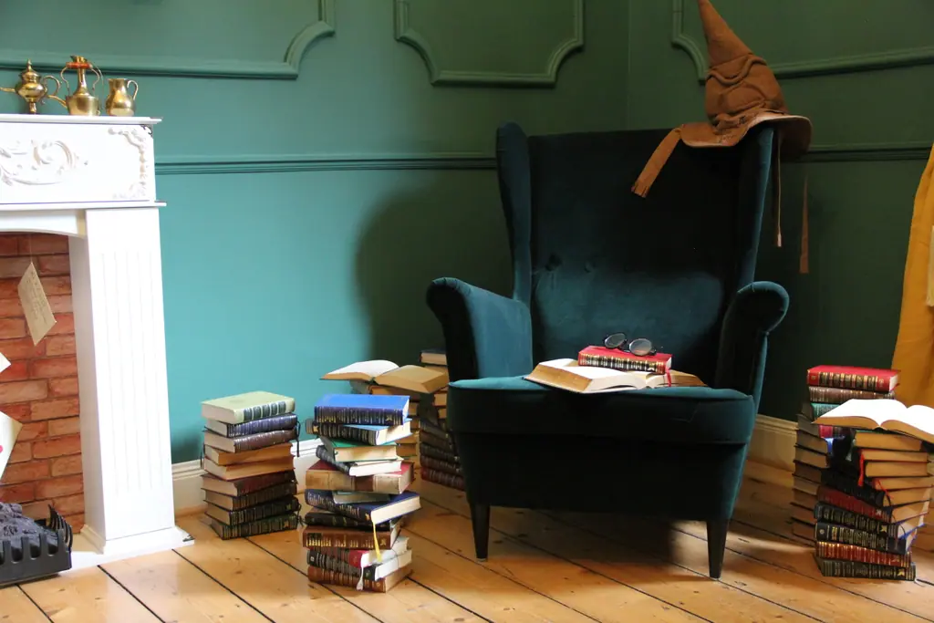 Dunkelgrüner Ohrensessel mit spitzem Hut, Bücherstapel und Lesebrille vor dem Kamin
