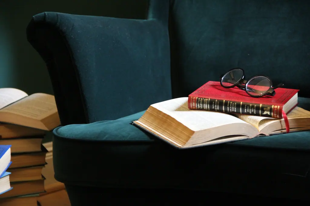 Aufgeschlagenes altes Buch mit runder Brille auf dem Samtsessel
