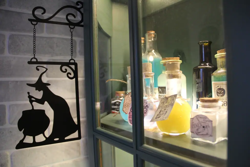 Hinterleuchtete Vitrine mit alten Flaschen und Zaubertränken, davor eine Hexen-Silhouette