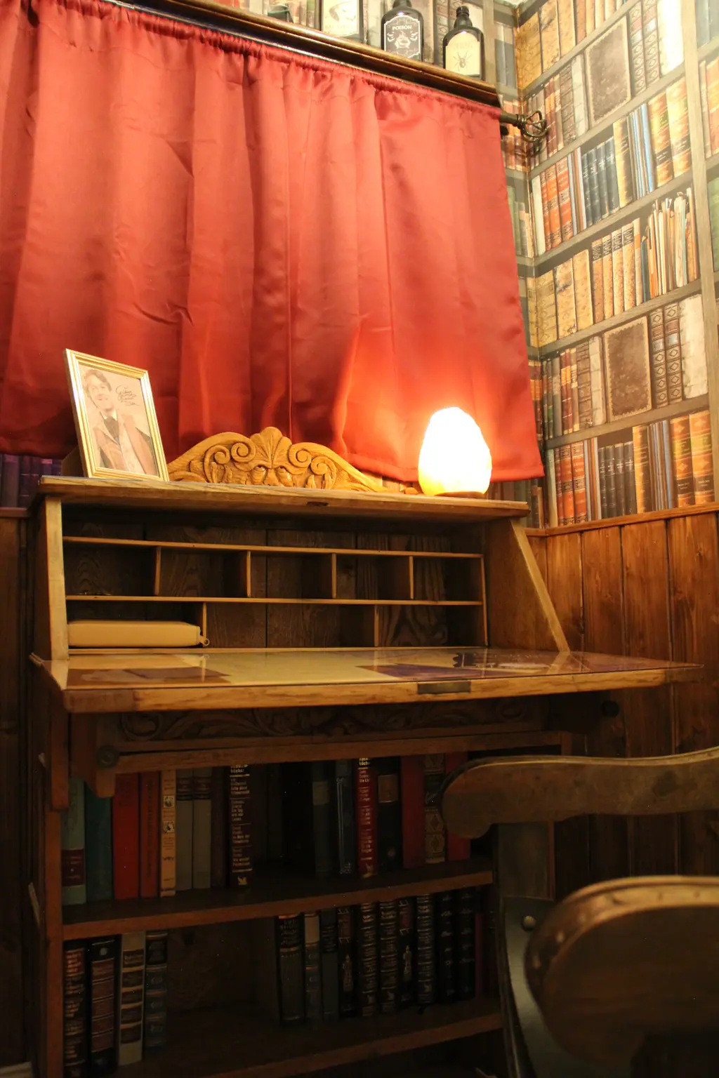 Leseecke mit altem Sekretär, Salzlampe und Bücherwand-Tapete hinter rotem Vorhang