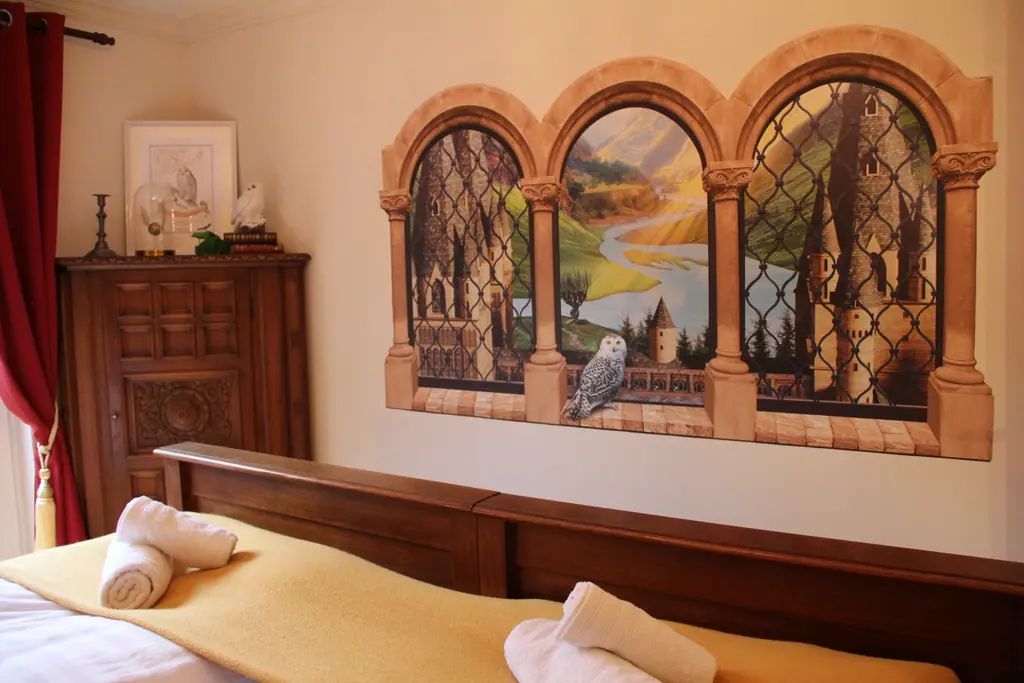 Schlafzimmer mit schwerem Holzbett, Wandbild mit Burgfenstern und gerollten Handtüchern