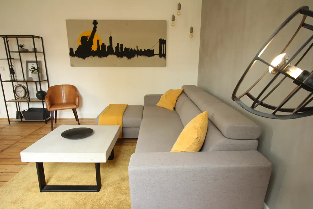Wohnzimmer des NY Loft: graues Ecksofa, gelbe Kissen, Betonwand und Skyline-Bild