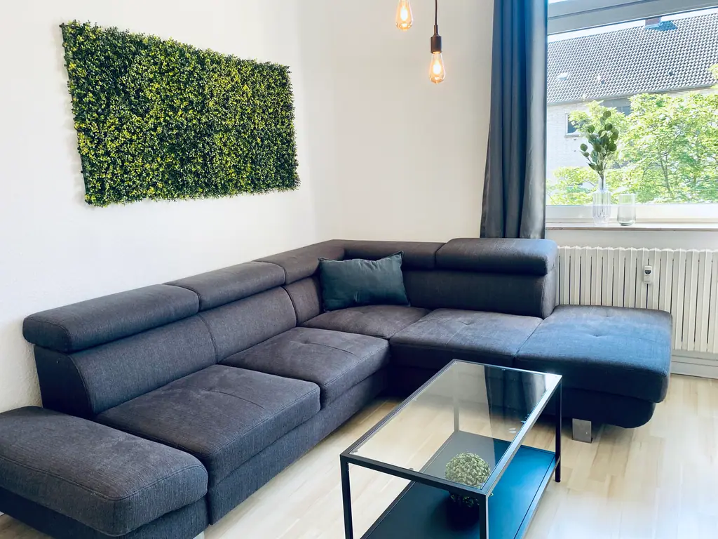 SH Team 3.0: graues Ecksofa mit Mooswand und Glühbirnenleuchte