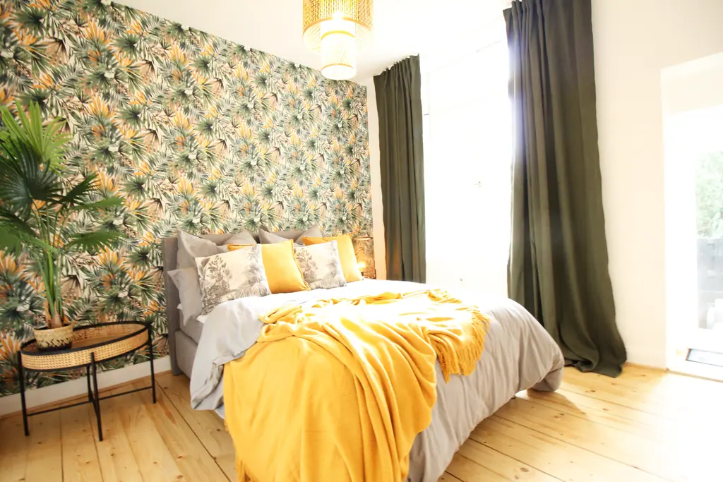 Schlafzimmer mit Dschungeltapete, gelber Tagesdecke und großem Fenster