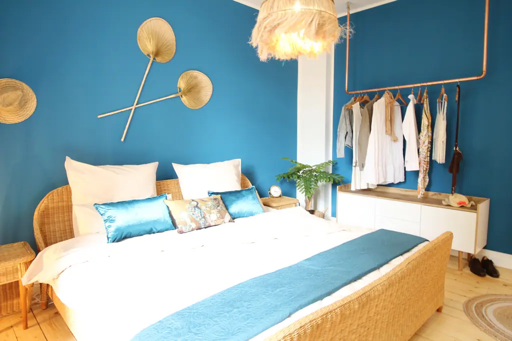 Bett vor blauer Wand mit Strohhüten als Wanddekoration